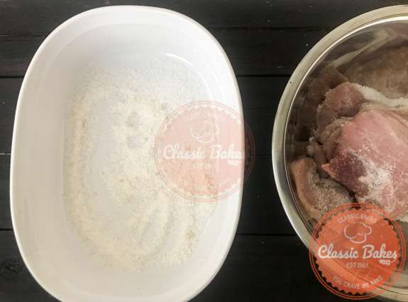 A layer of salt and sugar in a container next to a bowl of sliced pork  