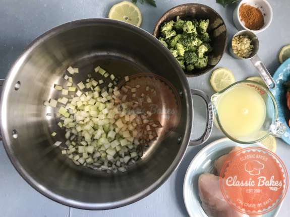 Onions and celery being added to a pot containing hot oil 