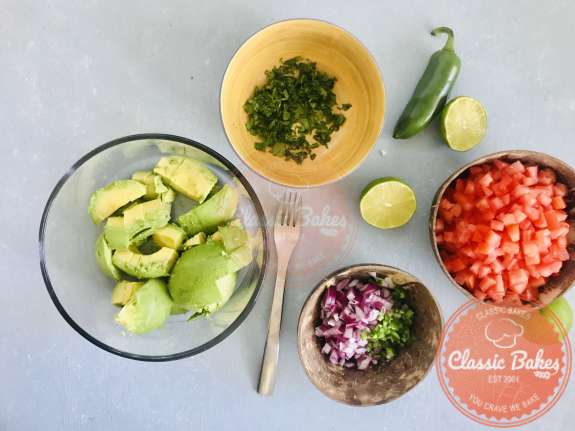 Overview of a avocado in a bowl next to Guacamole salsa ingredients 
