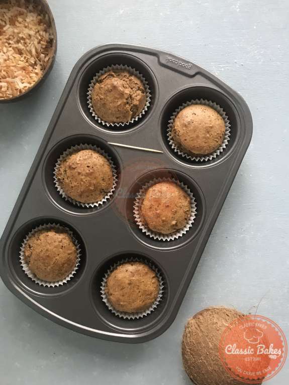 Overview of baked coconut cupcakes in a tin with a toothpick 