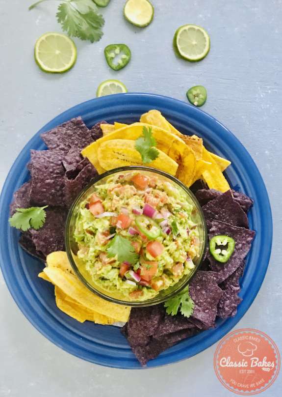 Overview of a bowl of Guacamole Salsa on a plate next to vegetable and tortilla chips 