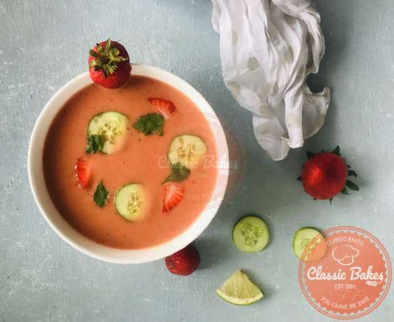 Overview of a bowl of strawberry soup garnished with cucumber, strawberries and cilantro. 