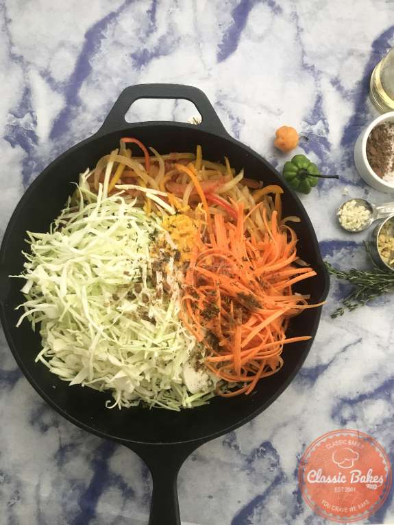 Overview of cabbage, carrots and scotch bonnet being added to a skillet 