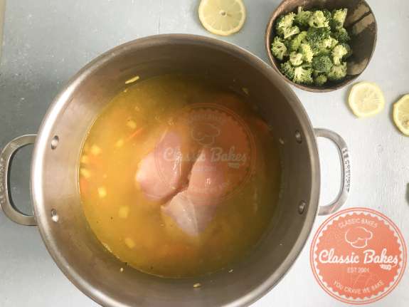 Overview of chicken broth and chicken breast being heated in a pot 