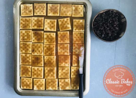 Overview of crackers with toffee being spread onto them using a spatula 