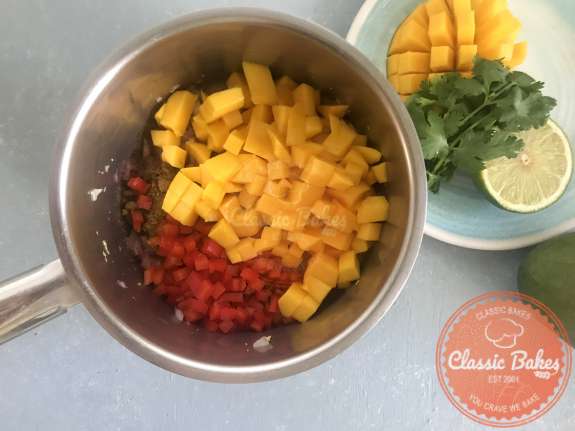 Overview of diced mangos, peppers and spices cooking in a pot. 