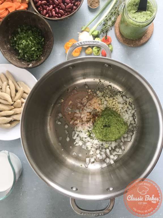 Overview of onions, garlic, herbs and green seasoning being added to a pot 