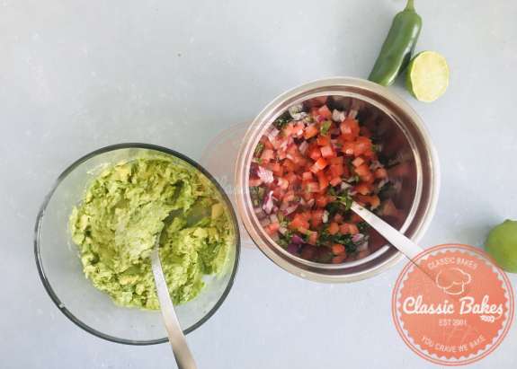 Overview of pico de gallo ingredients being mixed next of a bowl of mashed avocados 