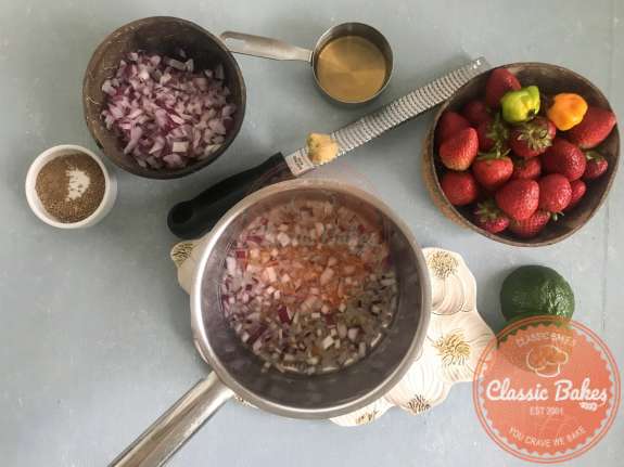 Overview of a pot containing red onions, water and scotch bonnet  
