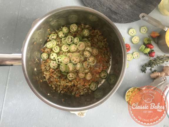Overview of a pot with fresh okra being added to it 