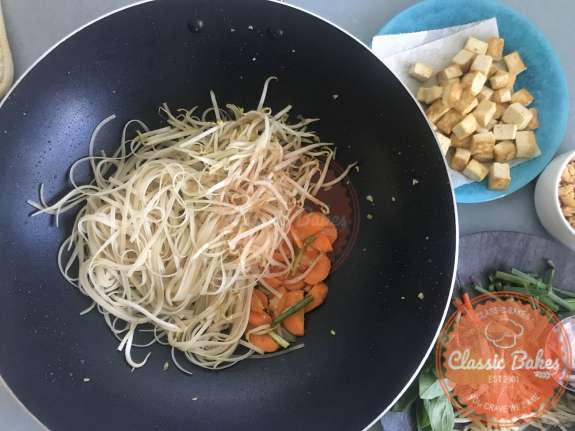Overview of rice noodles and bean sprouts being added to a wok 