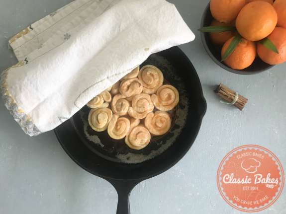 Overview of rolled orange rolls in a skillet with a kitchen towel covering them 