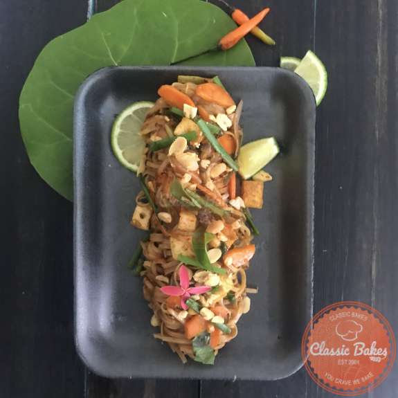 Overview of Tofu Pad Thai garnished with peanuts, Thai basil and lime wedges 