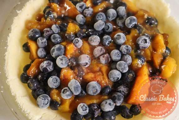 Peach blueberry filing being added to a pie shell. 