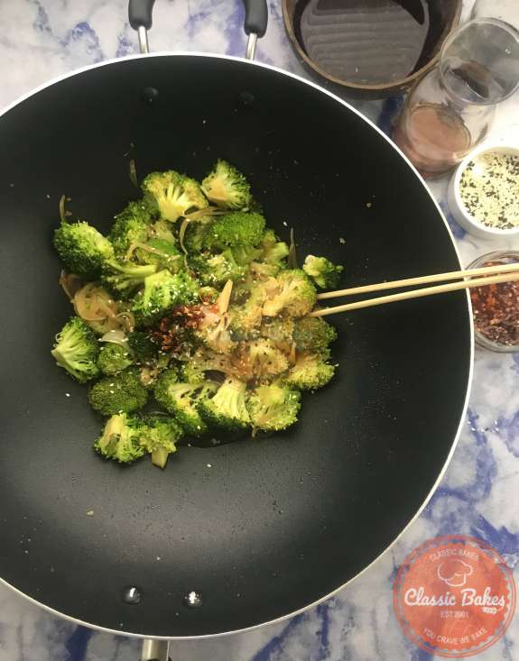 Sesame seeds and chili oil being stirred into broccoli with garlic sauce 