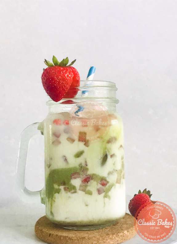 Side View of a Strawberry Matcha Latte with a straw inside, garnished with a strawberry on the rim of the glass