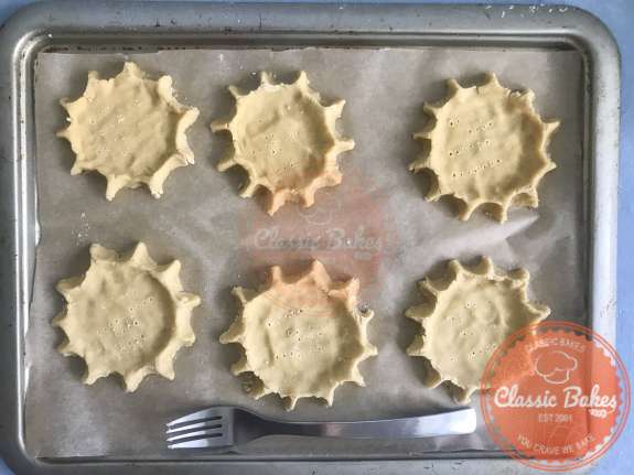A tray of tart shells being poked with a fork before going into the oven 
