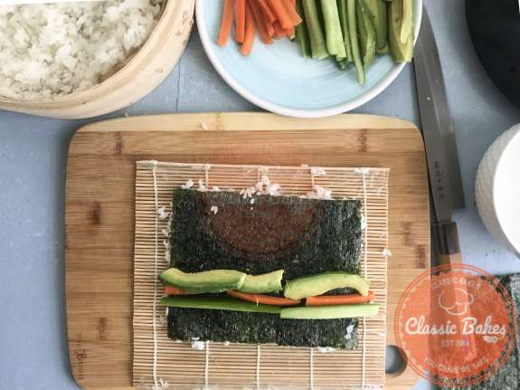 Vegetables being lined in on a sheet of nori and sushi rice 