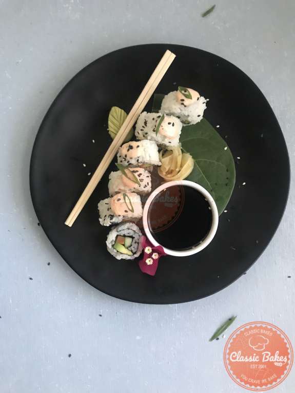 Veggie sushi roll on a plate with chopsticks, wasabi, ginger, scallions, spicy mayo and sesame seeds on it 