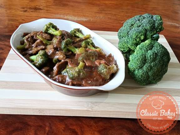 Sideview of a plate of instant pot beef and broccoli on a table next to broccoli crowns