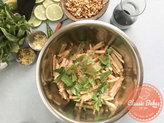 Mint, basil, noodles and seasonings being mixed into kohlrabi salad. 