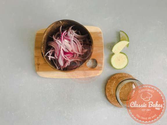 Overview of a bowl containing sliced red onions, lime and salt
