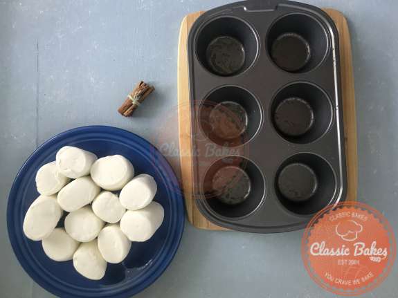 Overview of a muffin tin sprayed with cooking spray next to a plate of marshmallows
