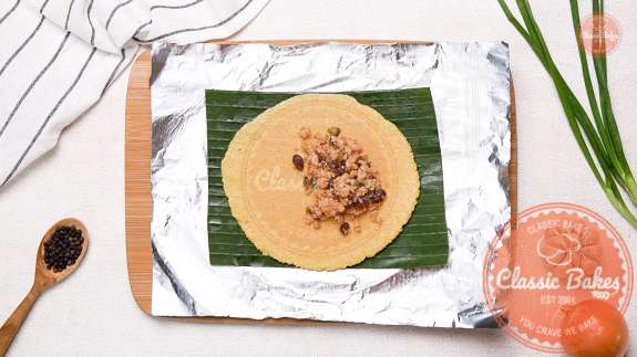 2 table spoons of pastelle filling added to a flattened dough on a banana leaf on top of foil