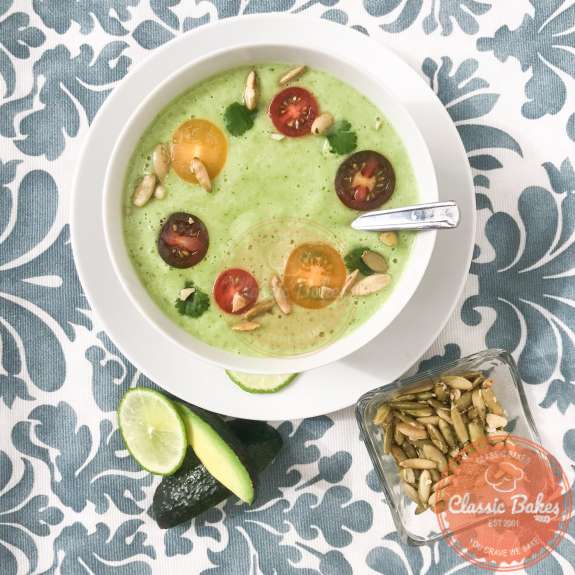 overview of a bowl of avocado soup garnished with tomatoes, cilantro and pumpkin seeds 
