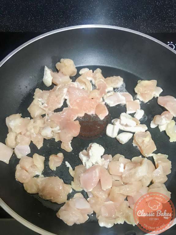 Diced chicken being browned in oil 