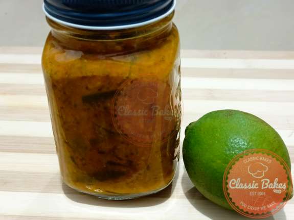 Side view of a jar on a tabletop filled with lime pickle next to a whole lime. 