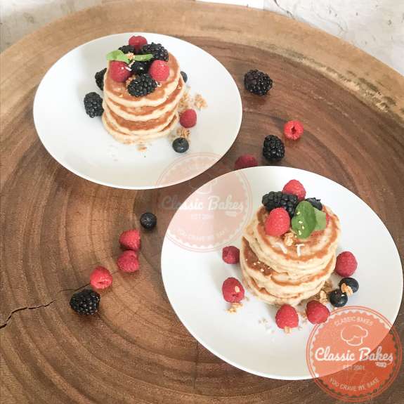 Side view of two plates of pancakes on a wooden table with berries 