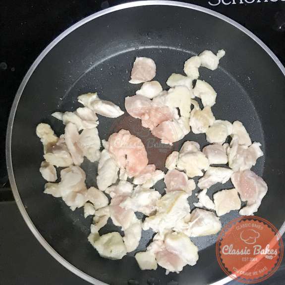 Overview of chicken being seared in a pan with oil 