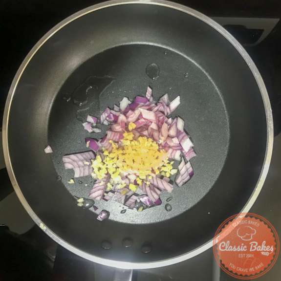 Overview of a hot pan with oil, red onions, garlic and ginger cooking