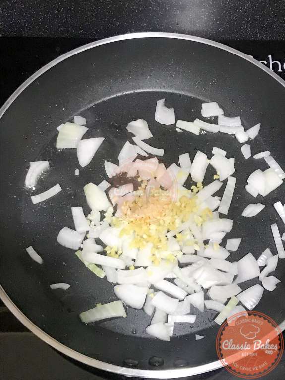 Overview of a pan with onions, garlic and ginger cooking inside 