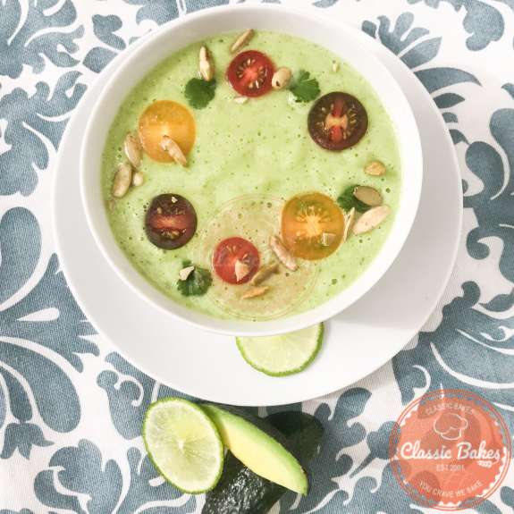Overview of a plated bowl of avocado soup with lime and avocado wedges on the side 