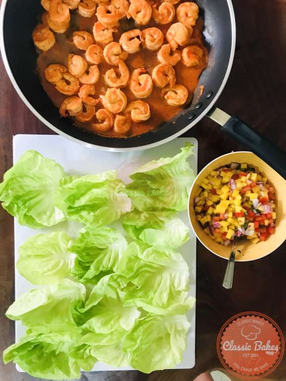 An overview shot of lettuce cups arranged on a cutting board next to a pan of buffalo shrimp and mango salsa