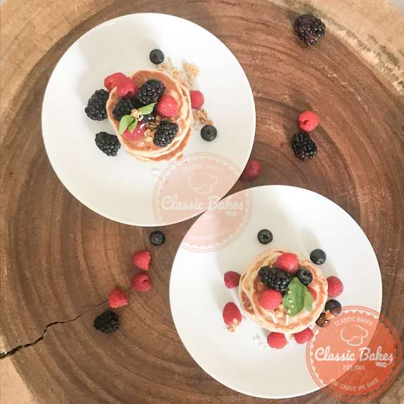 Overview of two stacks of pancakes garnished with berries on a wooden table 