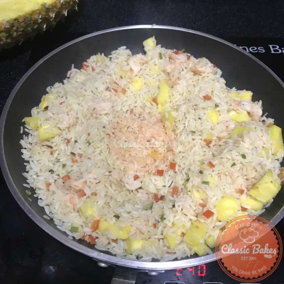 Pinapple and shrimp being mixed with rice and vegetables in a pan 
