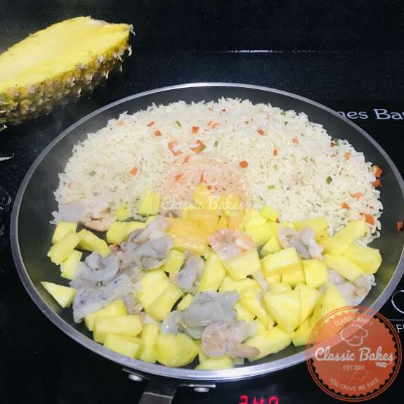 Shrimp and pineapple being cooked in a pan with rice 