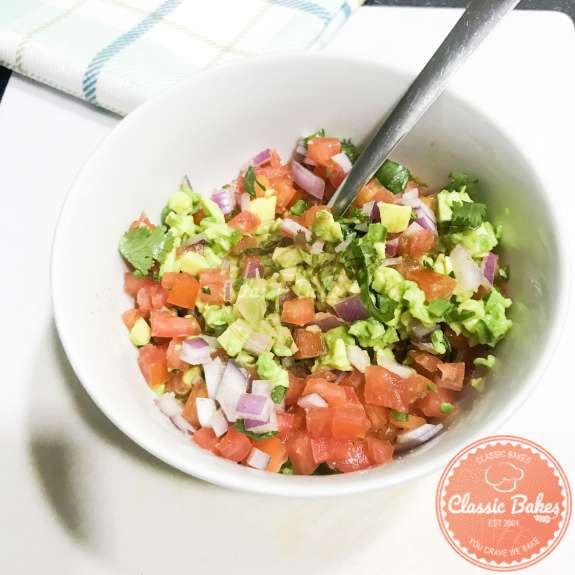 Side view of guacamole salsa being mixed together in a bowl with a spoon 