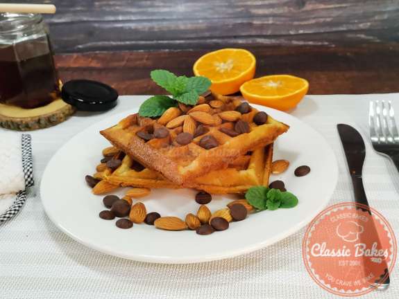 Side view of almond flour waffles on a plate garnished with chocolate and almonds. 