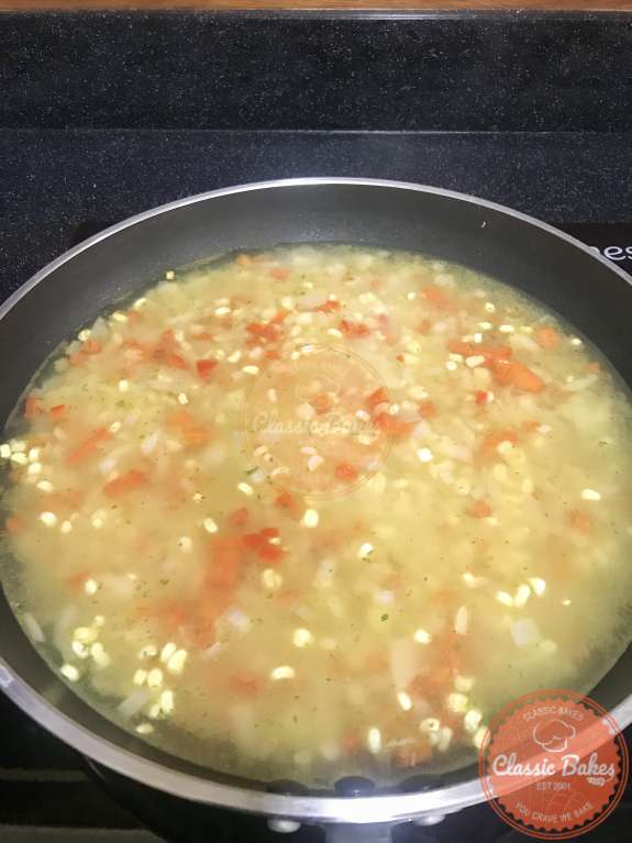 Vegetable stock being added to a pan of arroz con maiz. 