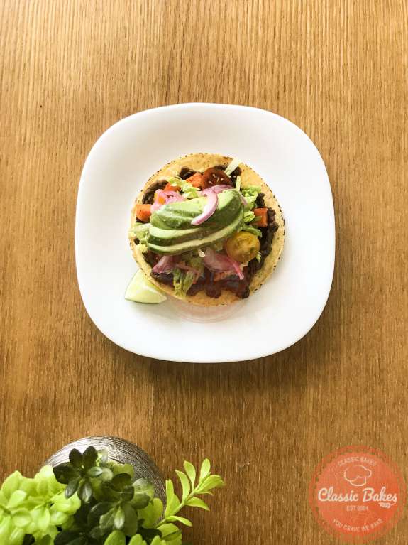 Overview of a plate with a garnished black bean tostada on a wooden table. 