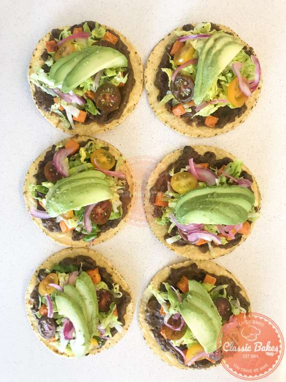 Overview of 6 garnished black bean tostadas on a kitchen countertop  