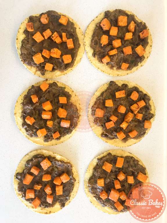 Overview of six tostada shells spread with refried black beans and roasted sweet potatoes