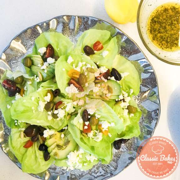 Top view of butter lettuce with tomatoes, olives, feta cheese, avocados and pumpkin seeds