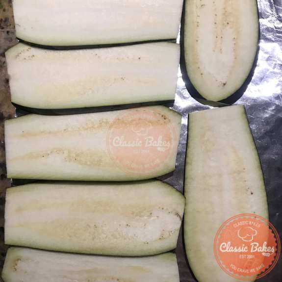Overview of slices of eggplant lined up on a baking sheet
