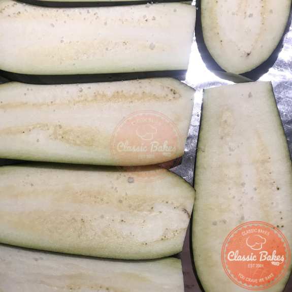 Overview of slices of eggplant sprinkled with sea salt on a baking sheet. 