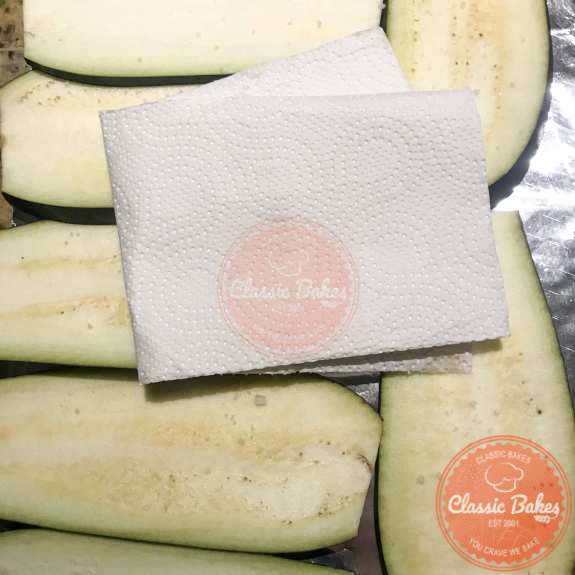 Slices of salted eggplant being patted dry using a paper towel 